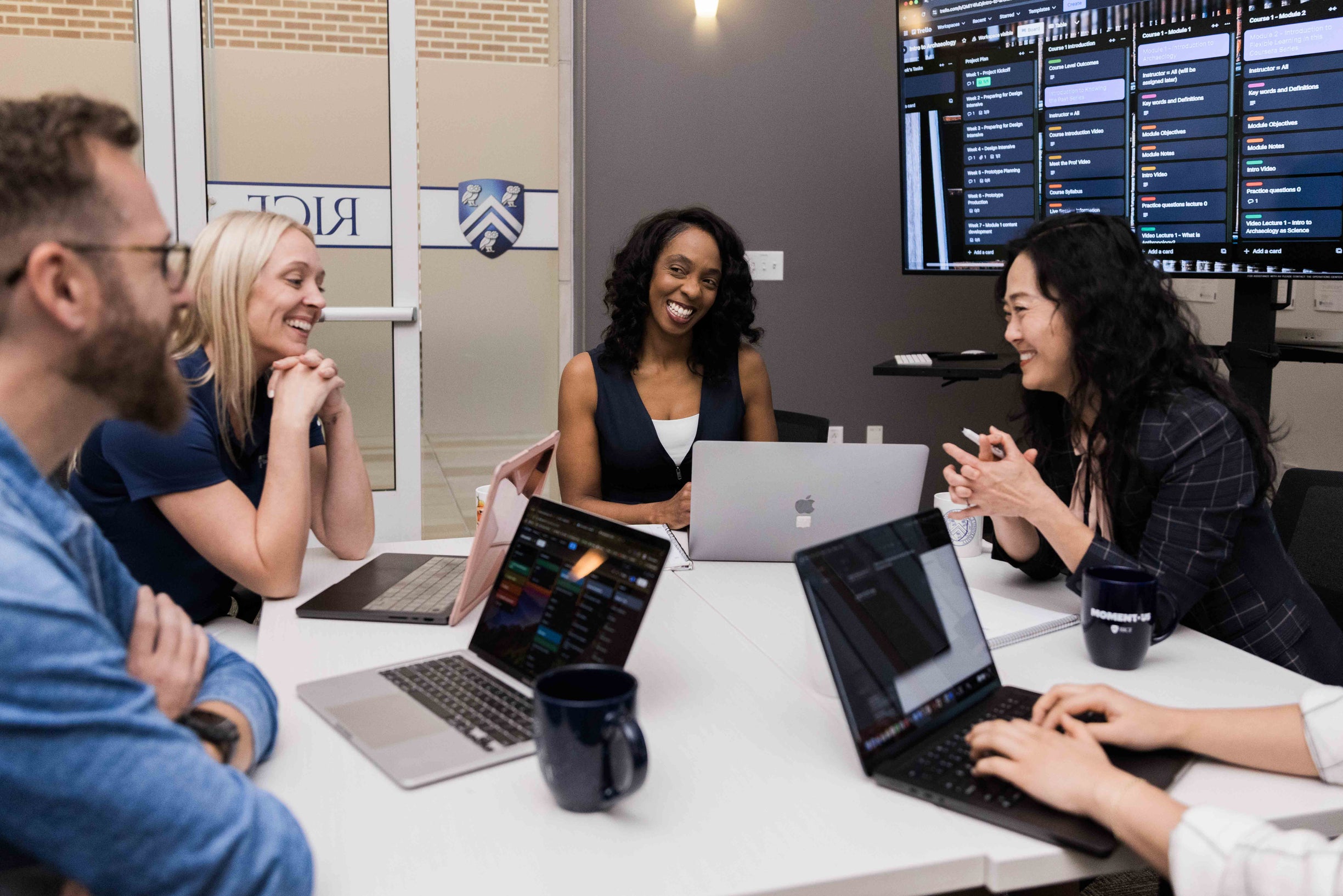 A diverse group of people seated around a table, each using laptops and engaged in discussion or collaboration.