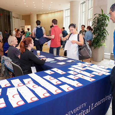 Students and staff gather around a Rice University Digital Learning registration table with name badges during a campus event.